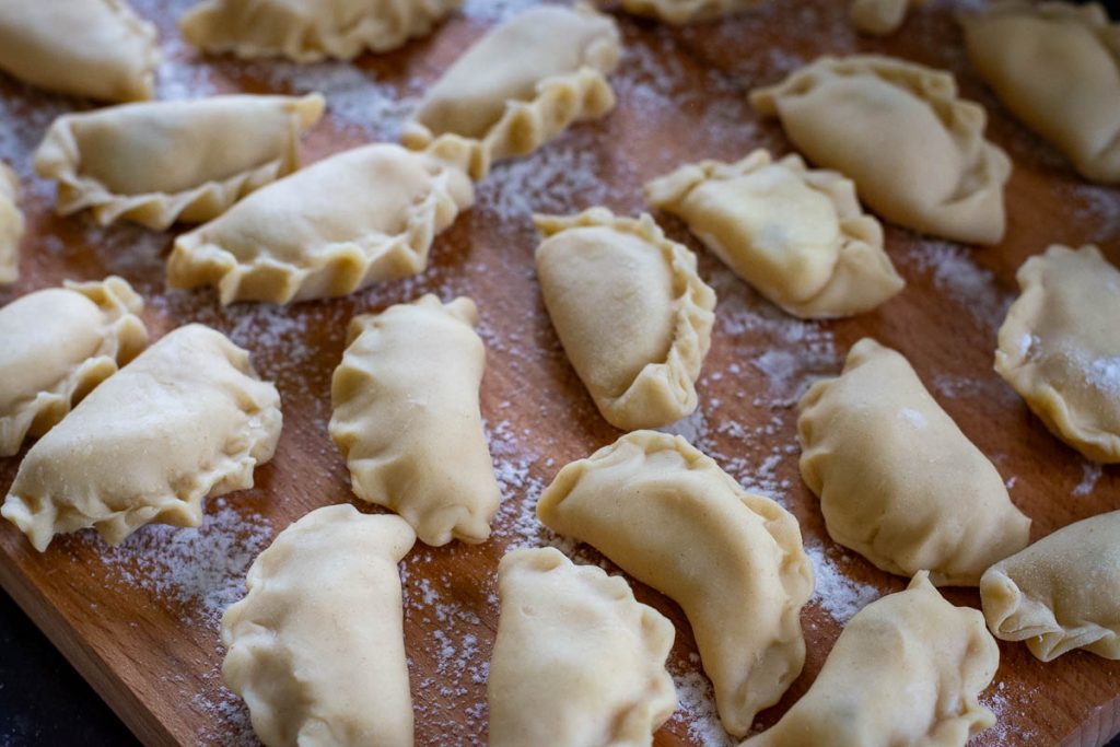Shaped Lithuanian dumplings on a floured wooden board.