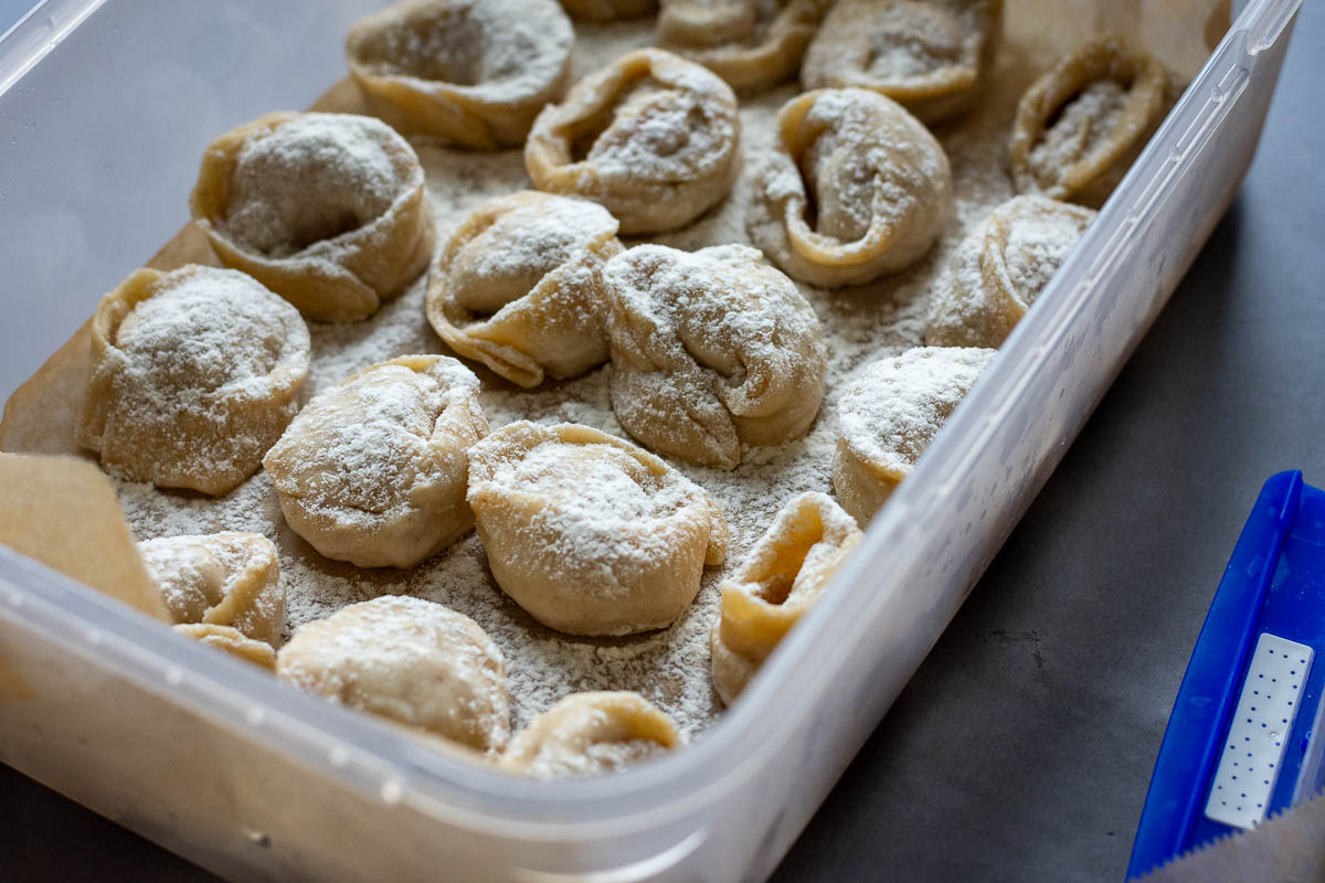 Shaped dumplings arranged in a single layer in a box lined with parchment paper. 