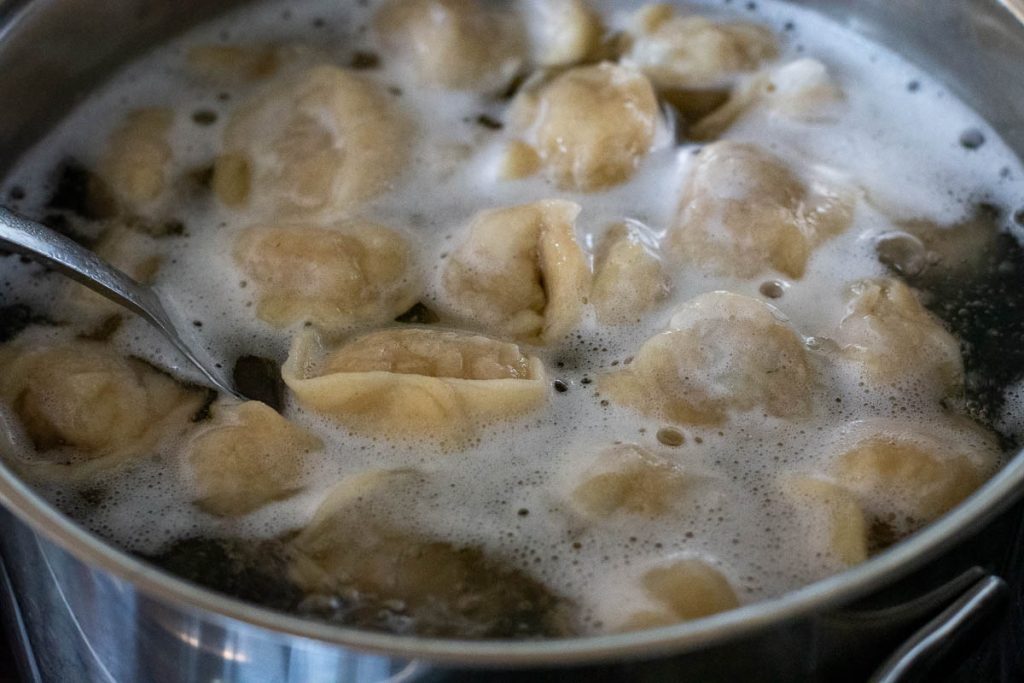 Lithuanian pork dumplings cooking in a pan of boiling water. 