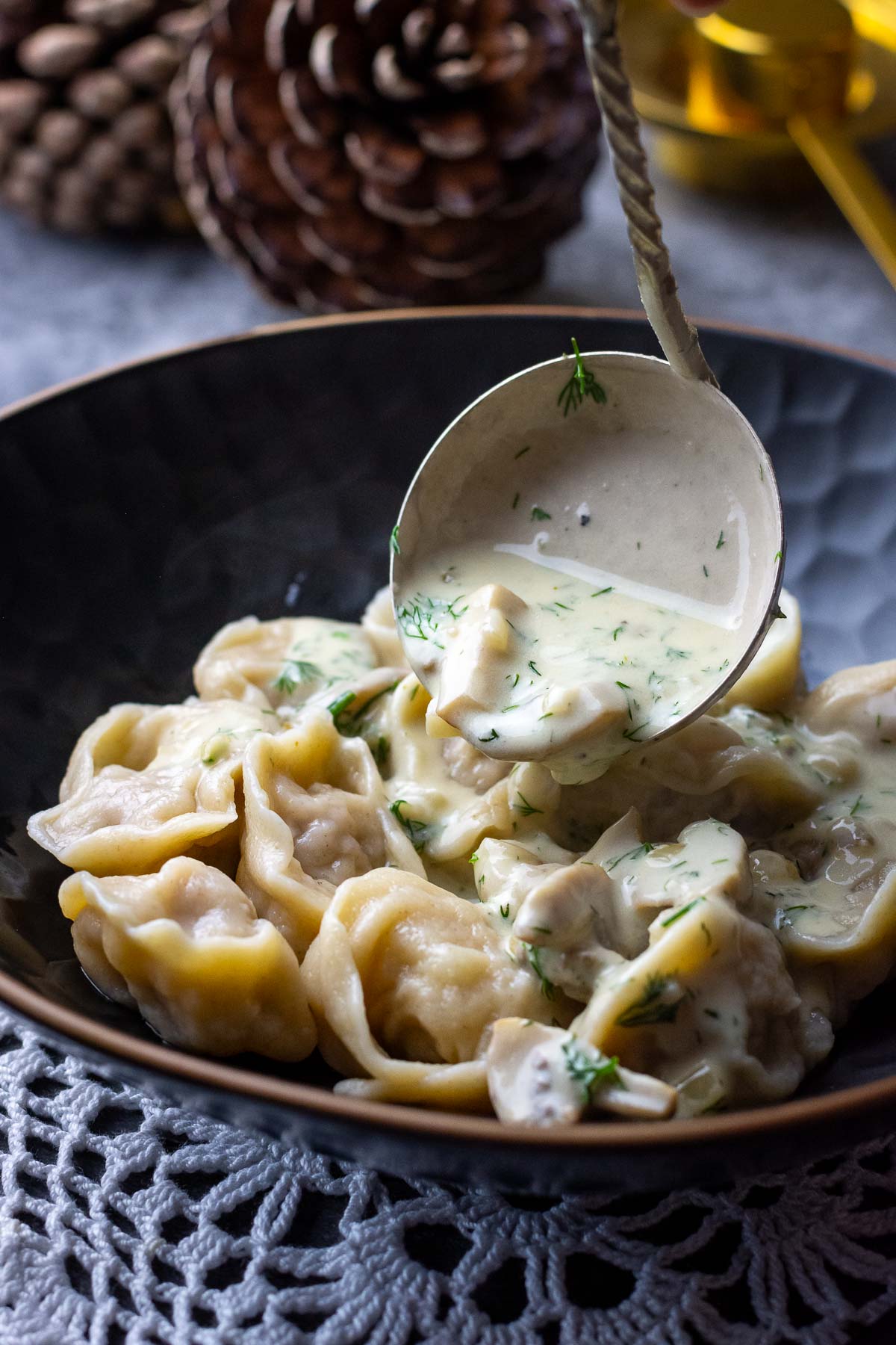 Mushroom sauce being ladled over the Lithuanian pork dumplings in a black bowl.