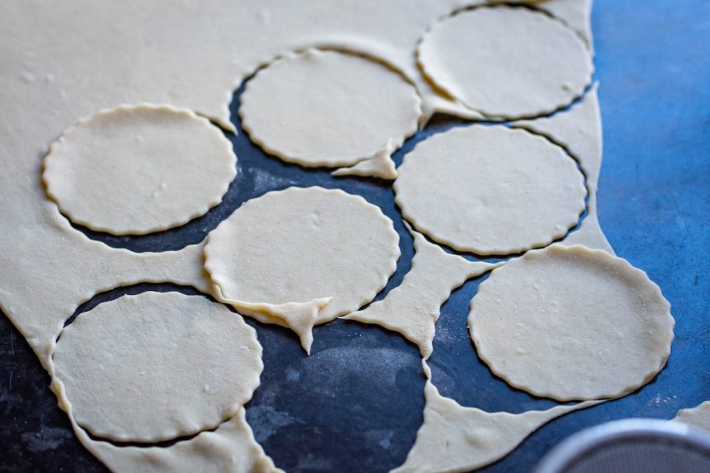 Stamping out circles of thinly rolled dough with a cookie cutter. 