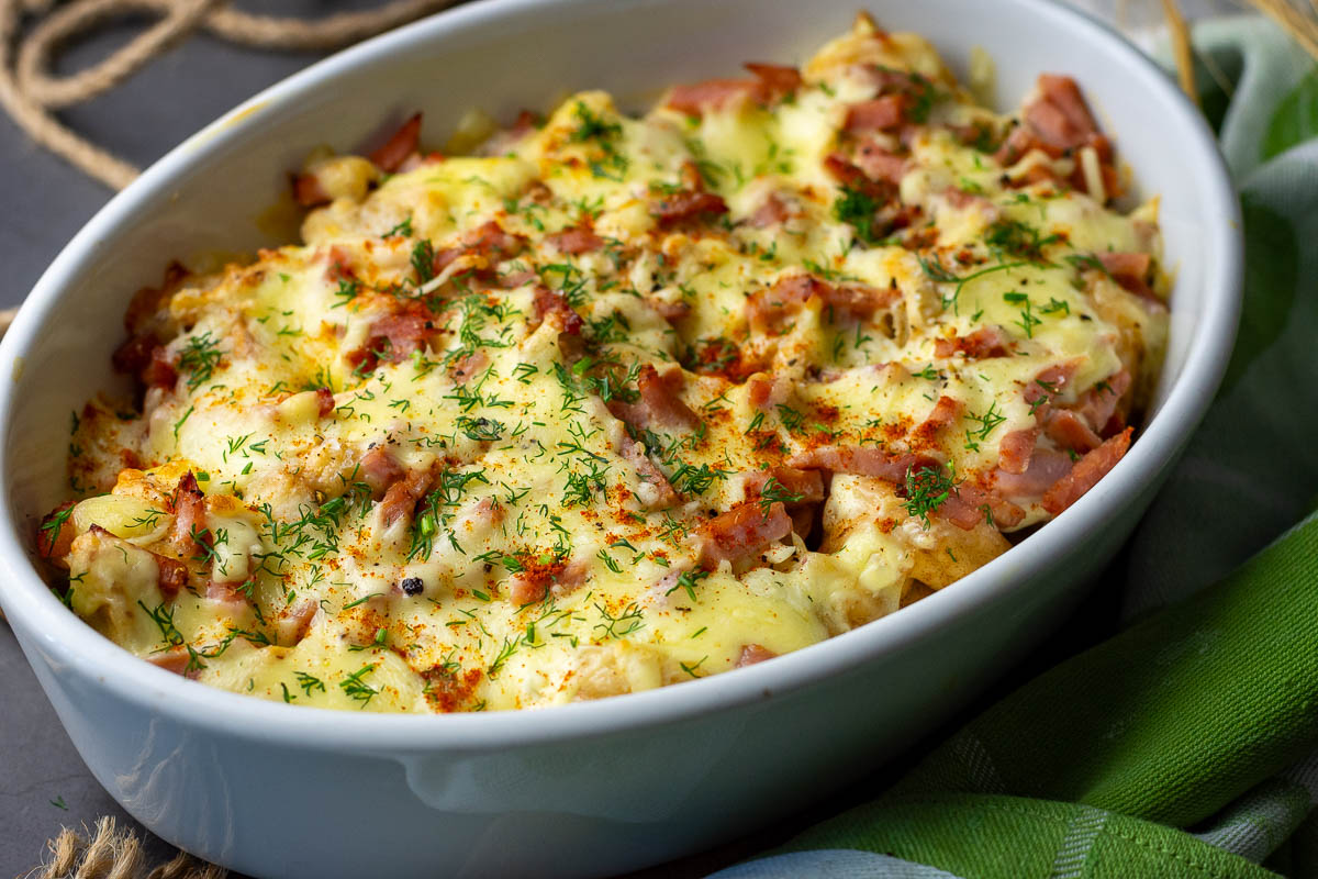 Fried pork dumplings baked under a sour cream, ham and cheese blanket in a white casserole dish. 