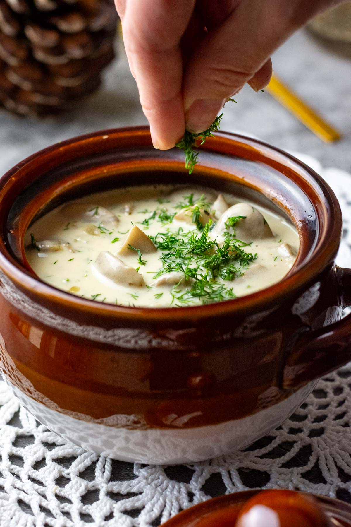 Sprinling fresh dill on top of Lithuanian mushroom sour cream sauce in a bowl.