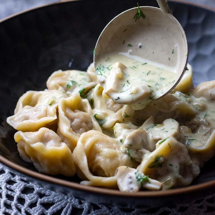 Mushroom sauce being ladled over the Lithuanian pork dumplings in a black bowl.