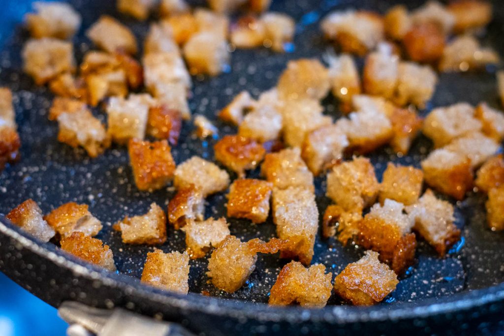Cubed bread being fried in a frying pan. 