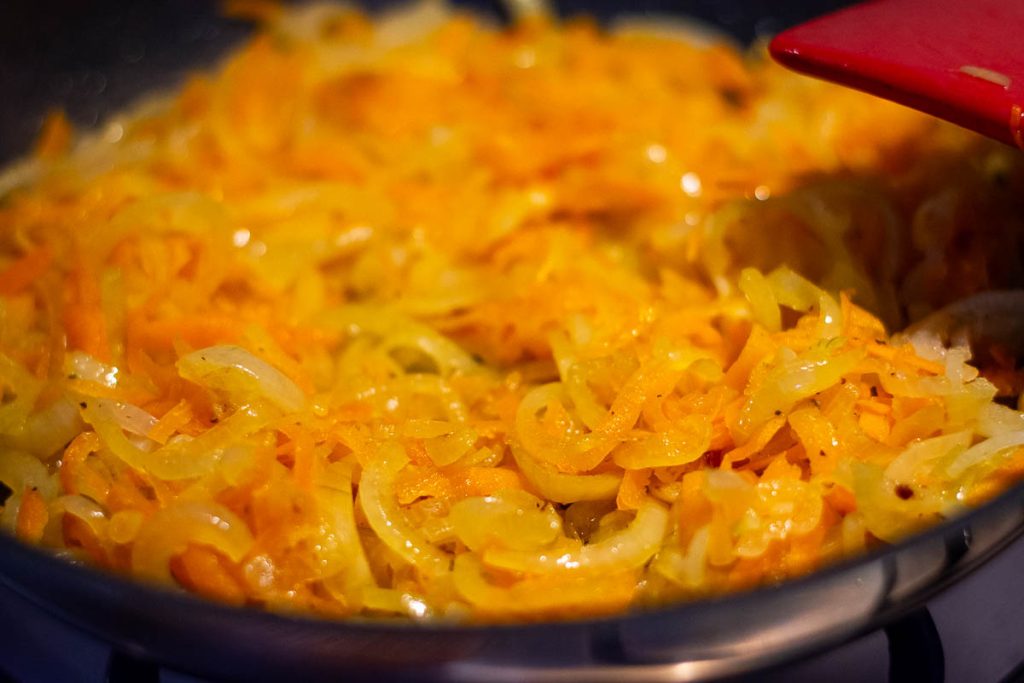 Carrots and onions softening in a frying pan.
