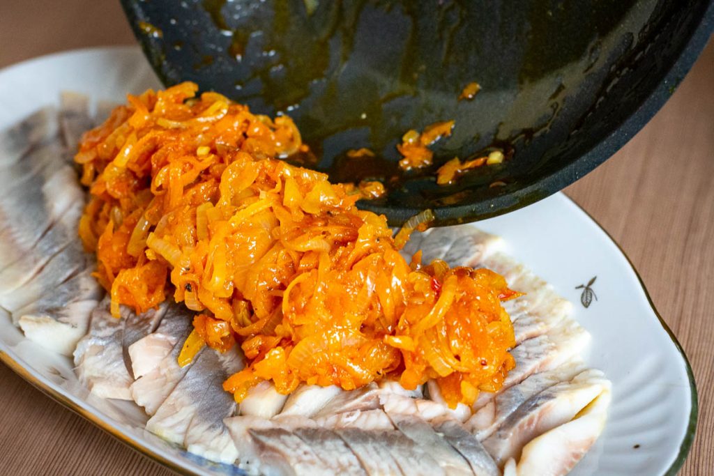 Adding the sauteed vegetables over the arranged slices of herring.