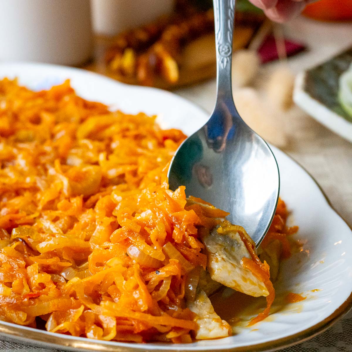 A piece of Lithuanian hering with onions and carrots on top being picked up with a spoon.