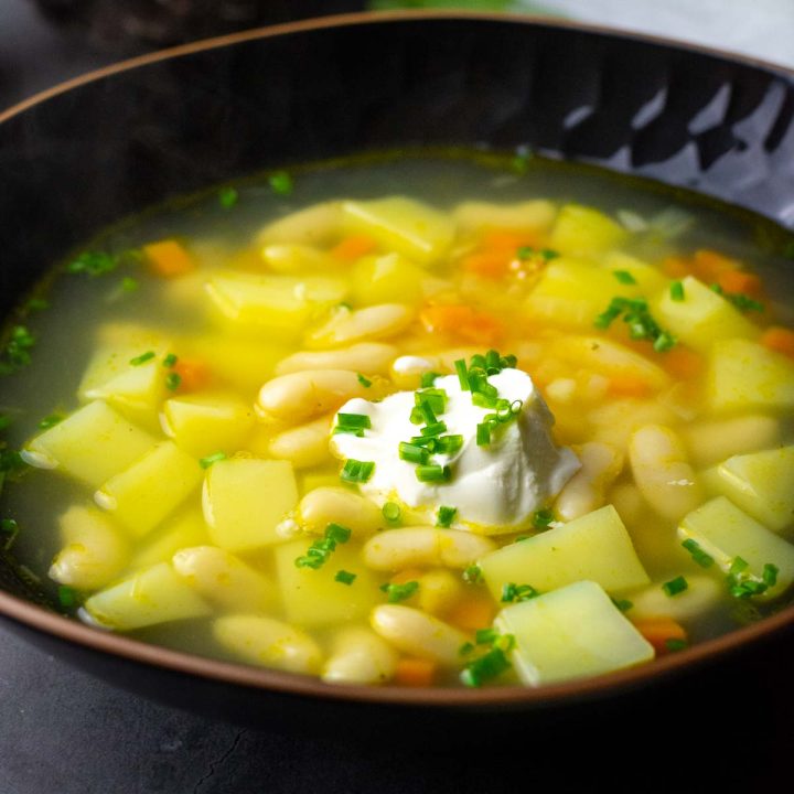 Lithuanian White Bean Soup With Potatoes in a black bowl.