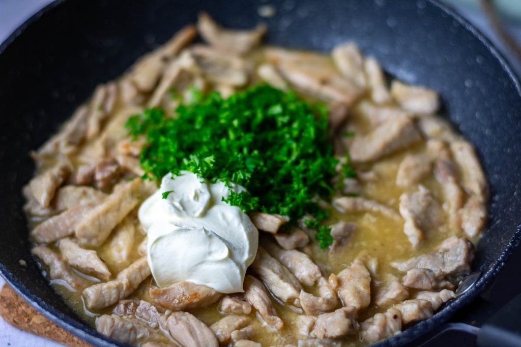 Parsley and sour cream being added to the pan with pork.