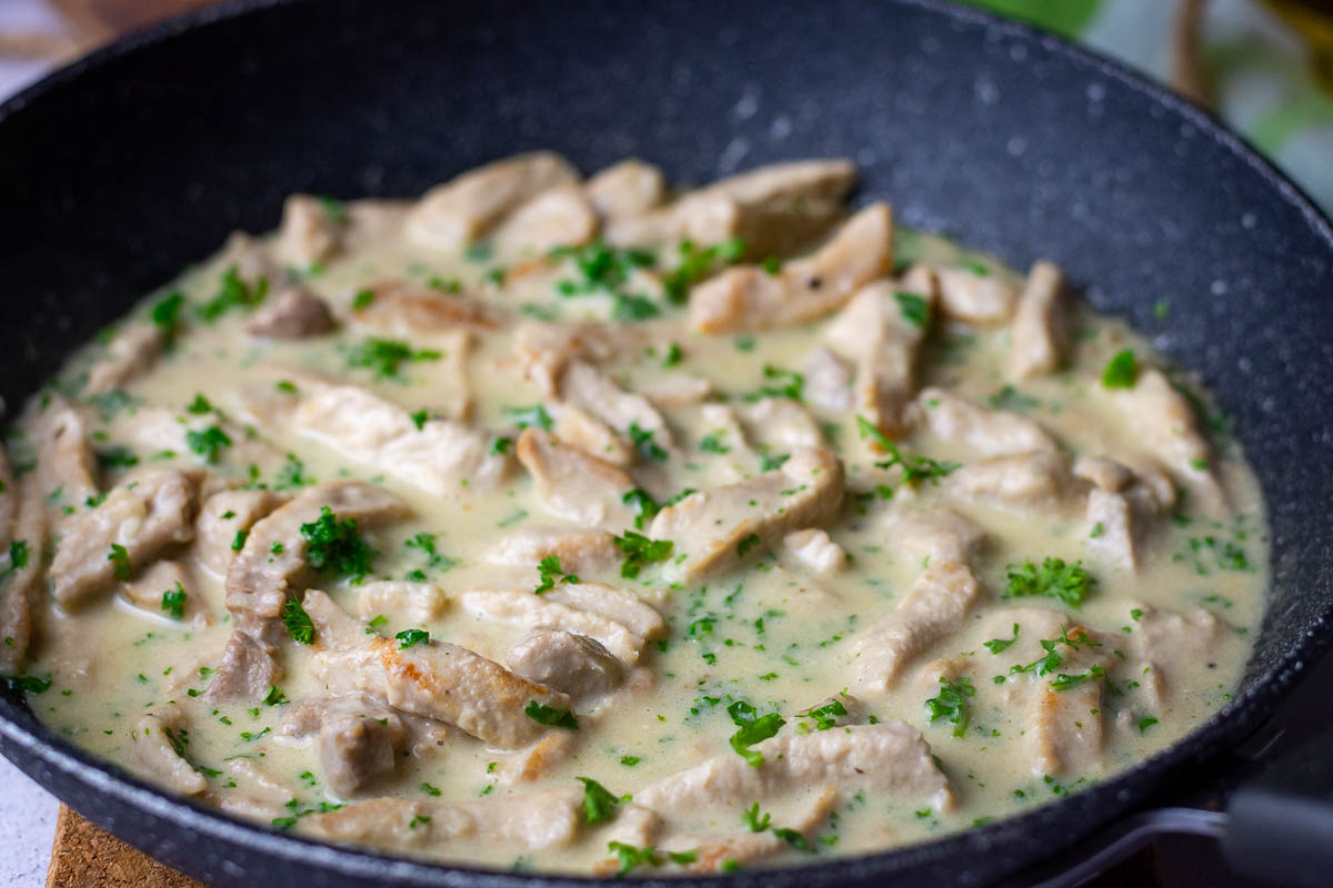 Lithuanian Pork in sour cream and parsley sauce in a pan being rehated.