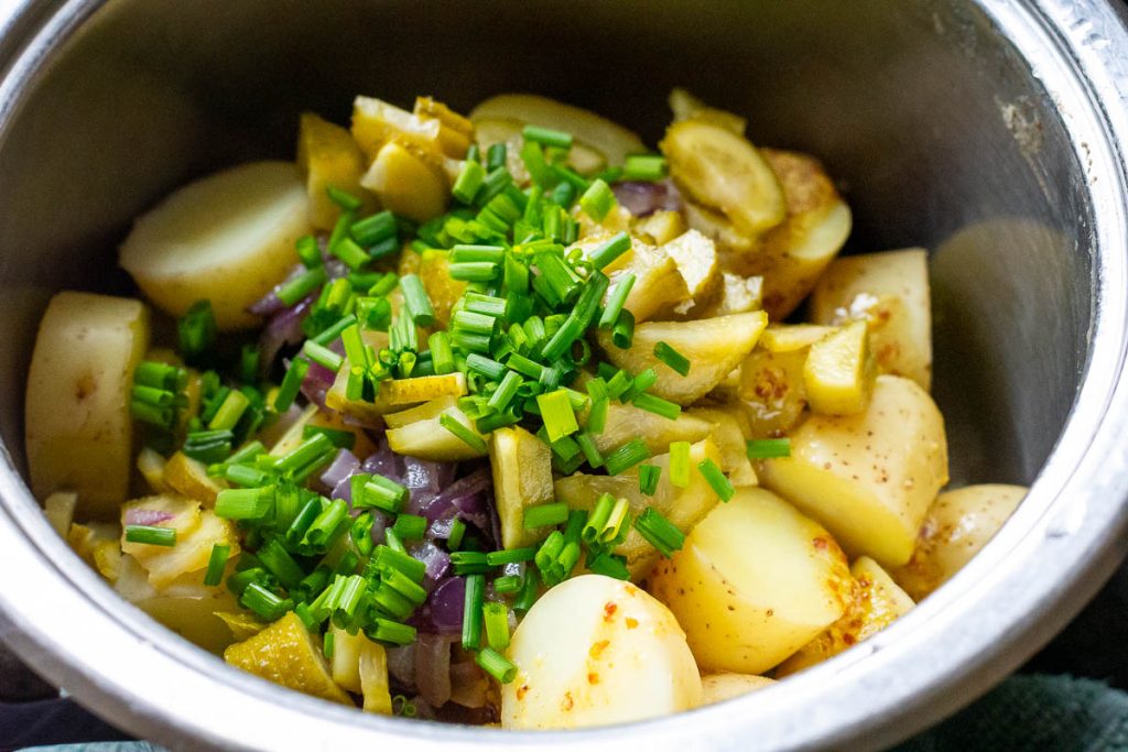 Cooked potatoes being mixed with chives and sauteed onions.
