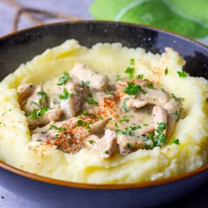 Creamy Lithuanian pork in sour cream sauce on a bed of mashed potatoes.