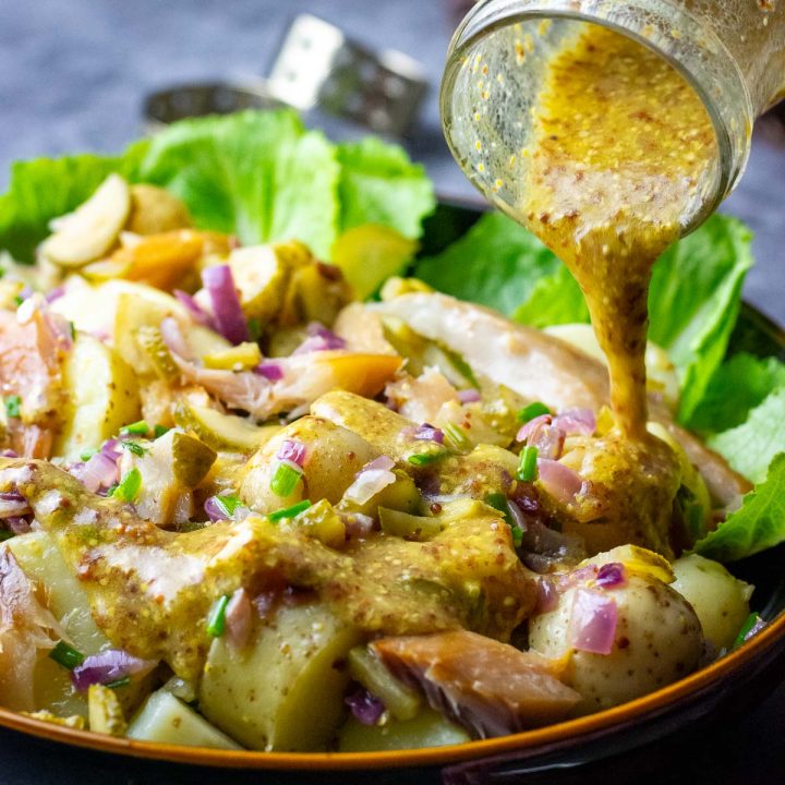 Wholegrain mustard dressing being poured over Lithuanian Potato and Smoked Mackerel Salad.