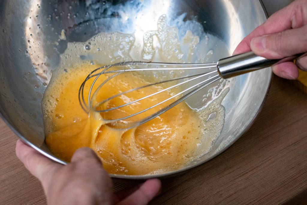 Whisking wet ingredeints in a large metal bowl with a balloon whisk.