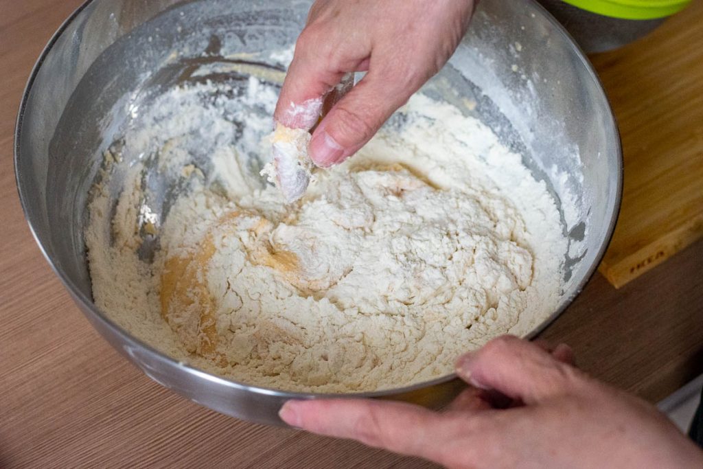 Mixing the dough with hands in a metal bowl.