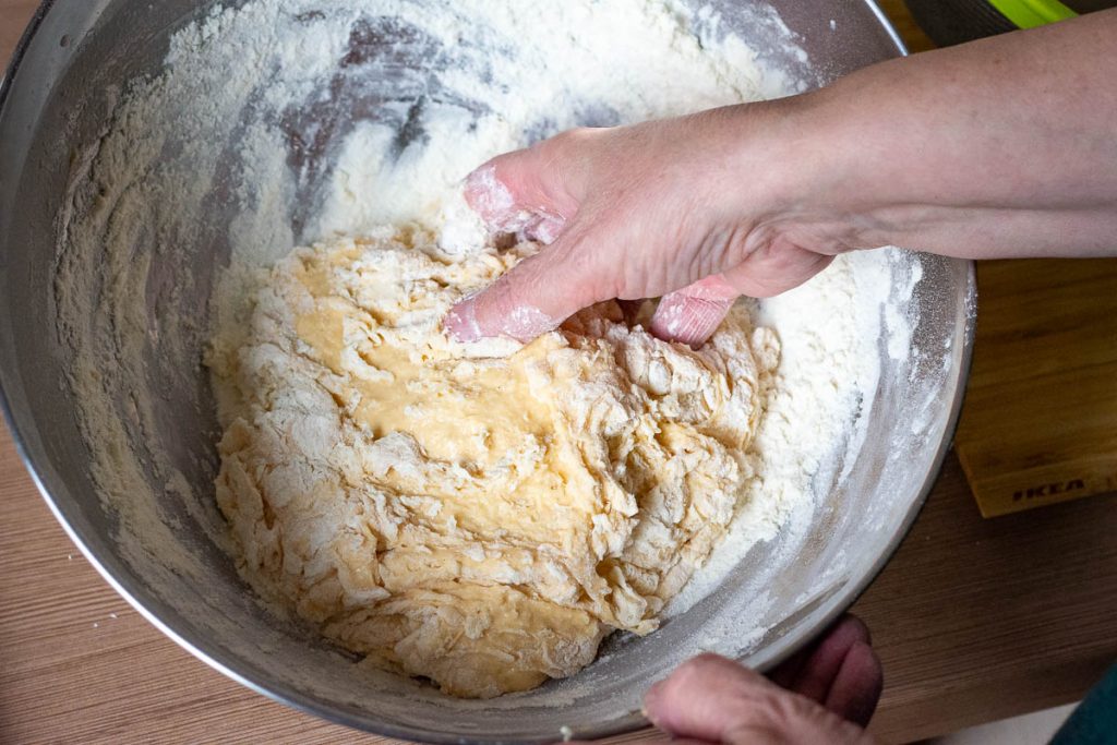 Mixing the dough with hands in a metal bowl.