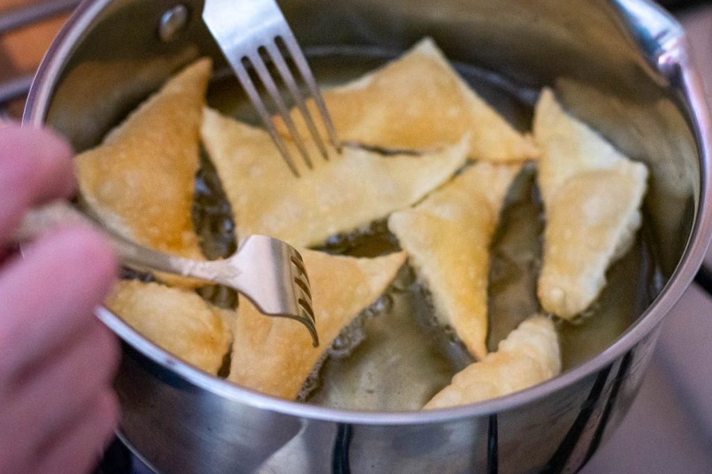 Flipping pastry pieces in hot oil with two forks.