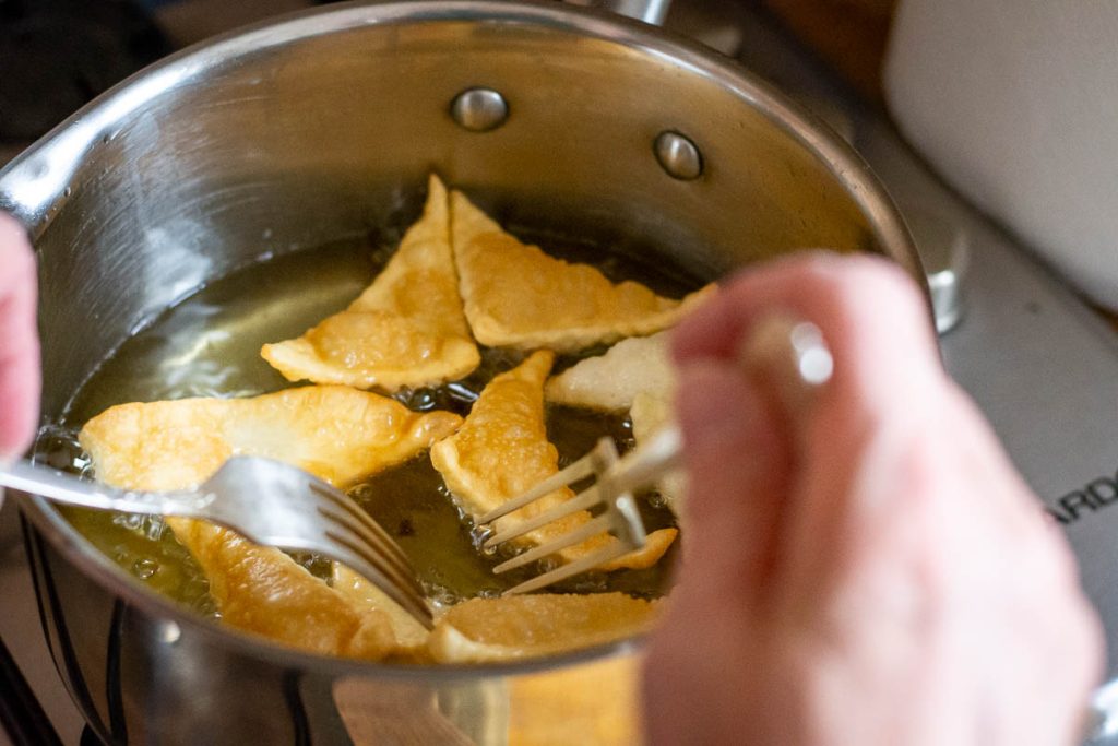 Flipping pastry pieces in hot oil with two forks.