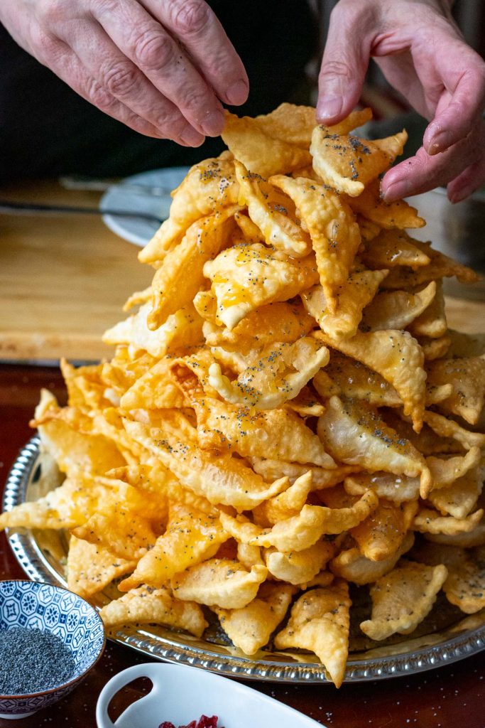 Stacking fried pastry triangles with layers of honey glaze and poppy seeds to glue them together.