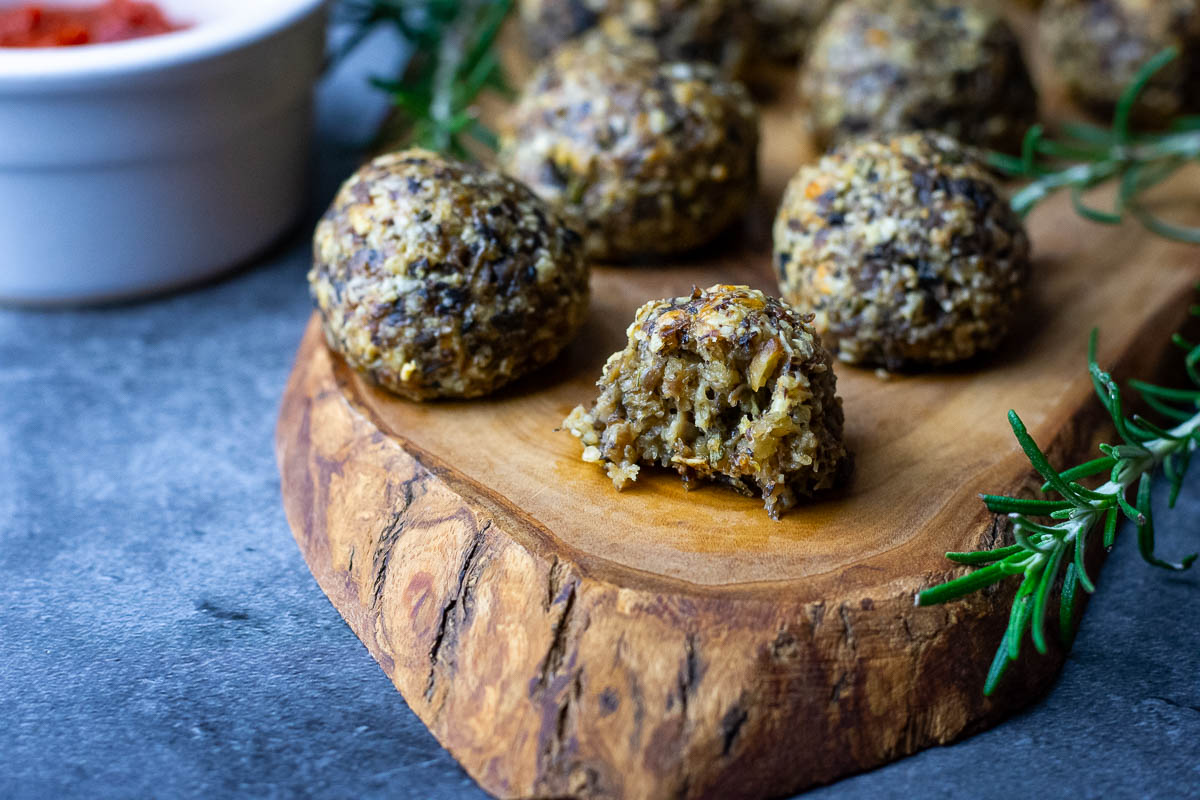 Lithuanian meatless mushroom balls on a decorative wooden board with one of the balls bitten into. 