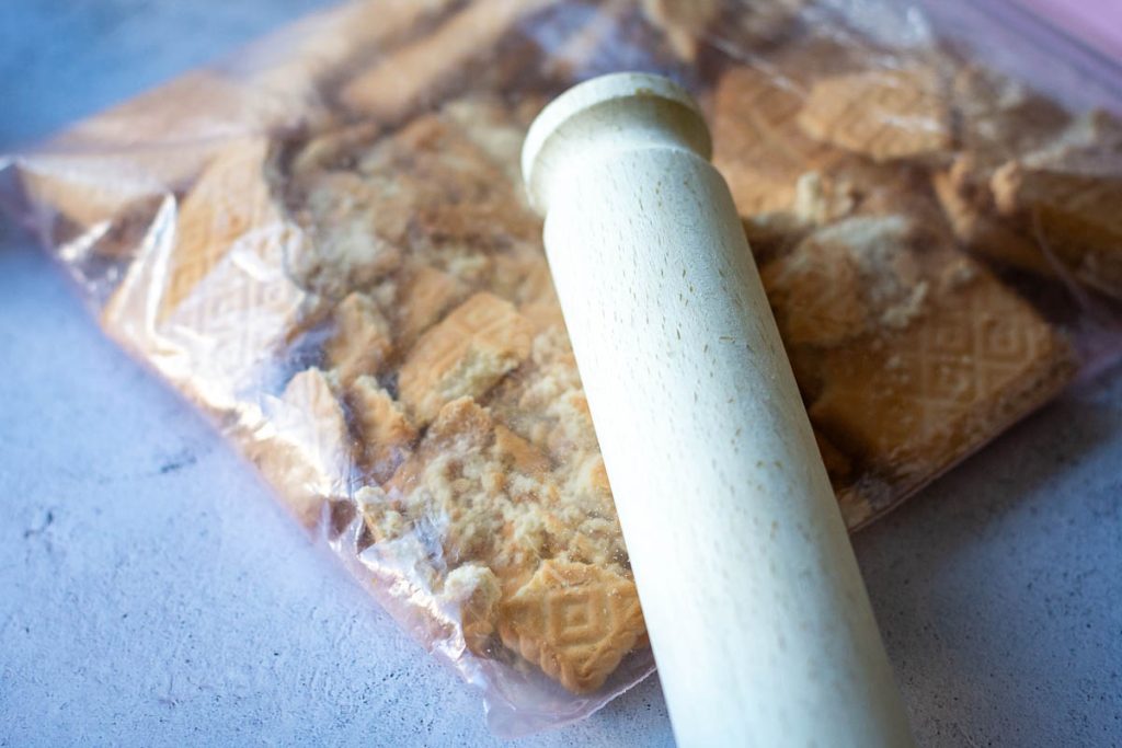 Crushing plain cookies in a ziplck bag with a wooden rolling pin.