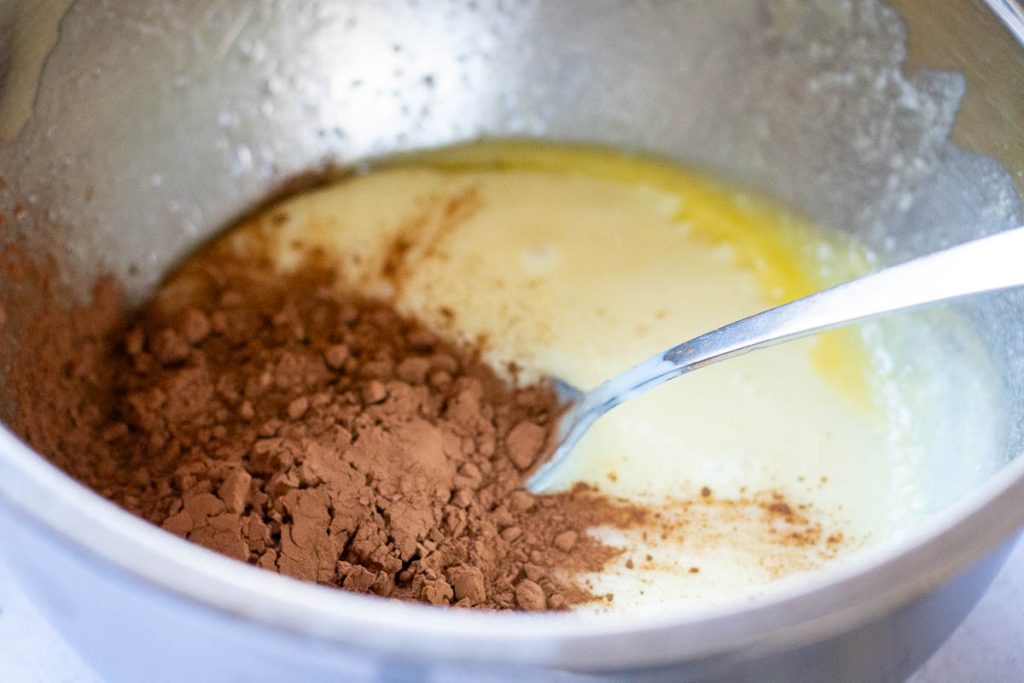 Condensed milk, melted butter and cocoa powder being mixed in a bowl.