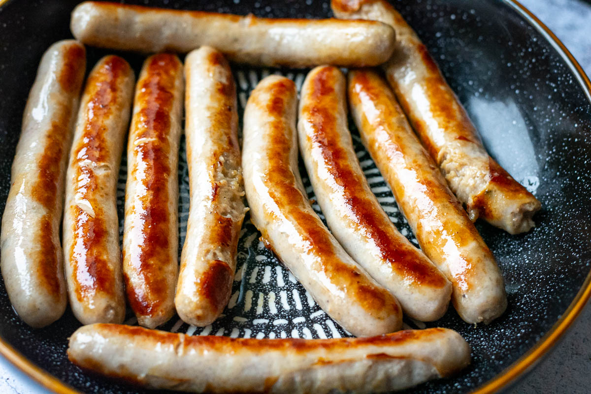 Browned chipolata sausages in a bowl.