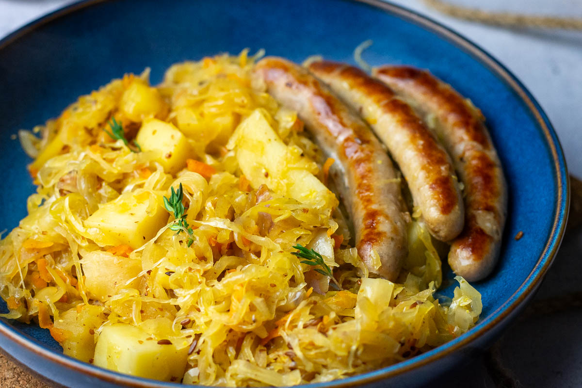 Lithuanian sauerkraut with potatoes and sausages served in a blue bowl.