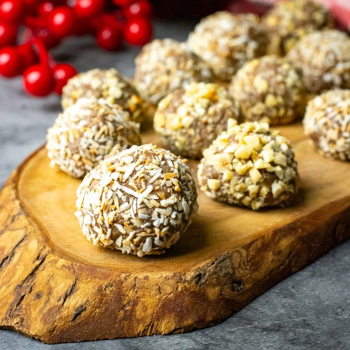 Lithuanian Chocolate Truffles with condensed milk rolled in toasted coconut and chopped roasted hazelnuts on a decorate wooden board.