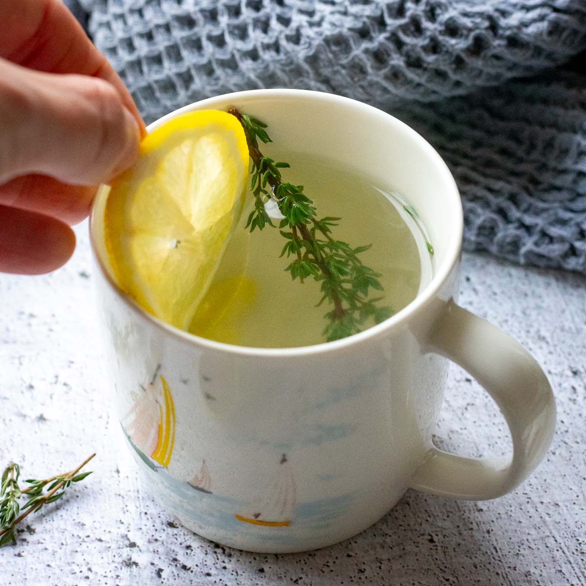 A slice of lemon being added to a cup of Lithuanain Thyme Tea. 