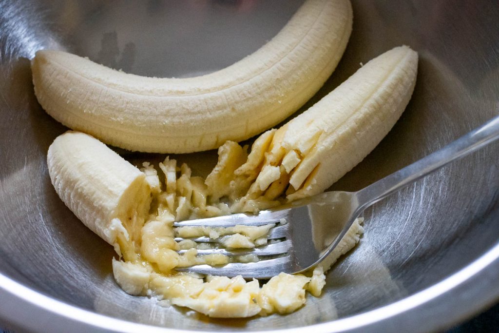 Mashing banana with a fork in a large bowl. 