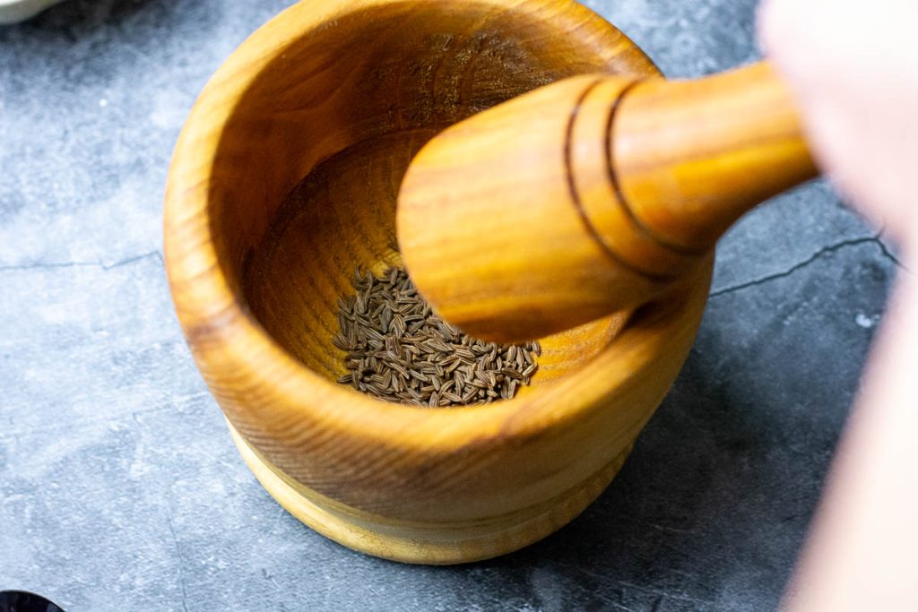 Caraway seeds in a wooden pestle and mortar.