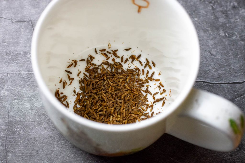 Lightly crushed caraway seeds in a mug. 