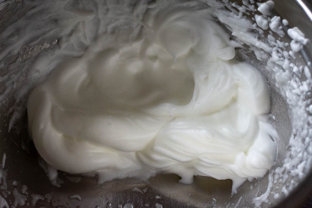 Egg whites whisked to medium peaks in a metal bowl.