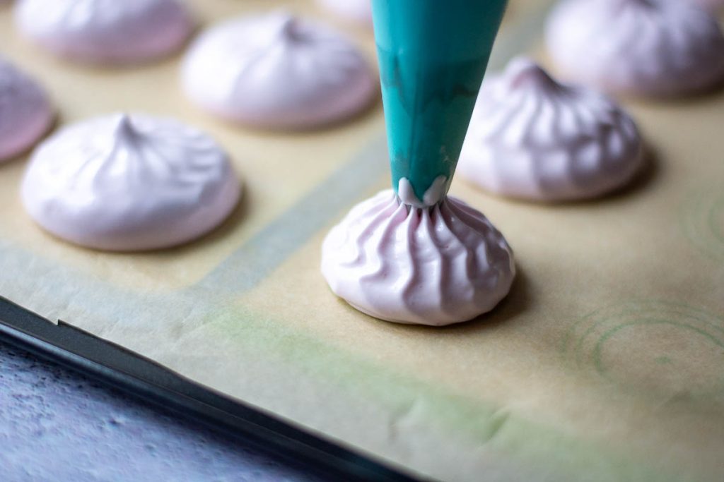 Piping marshmallows on a baking sheet lined with parchment paper.