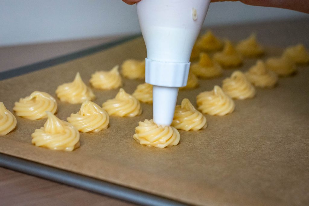 Piping the choux pastry dough onto a parchment paper lined baking sheet.