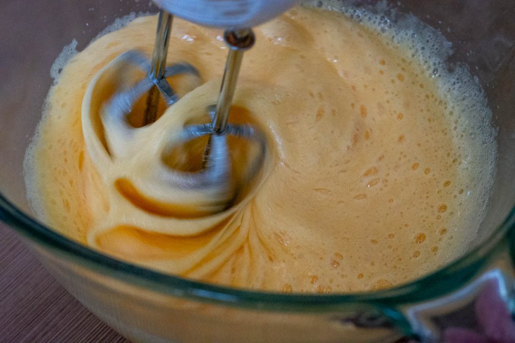 Whisking eggs and sugar using an electric handheld mixer.