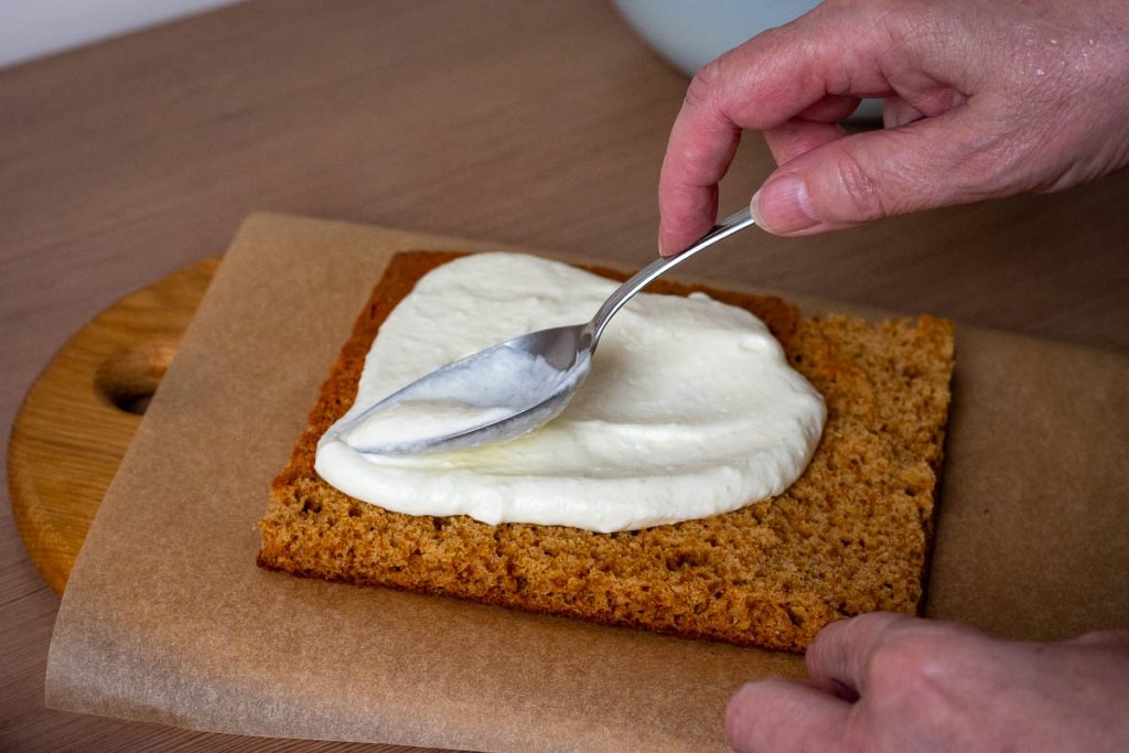 Assembling Lithuanian Honey Cake Sodzius by layering sponge, sour cream filling and jelly cubes.