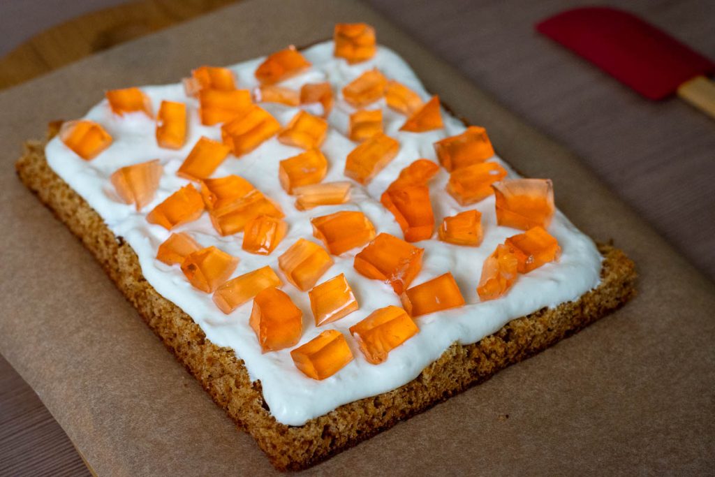 Assembling Lithuanian Honey Cake Sodzius by layering sponge, sour cream filling and jelly cubes.