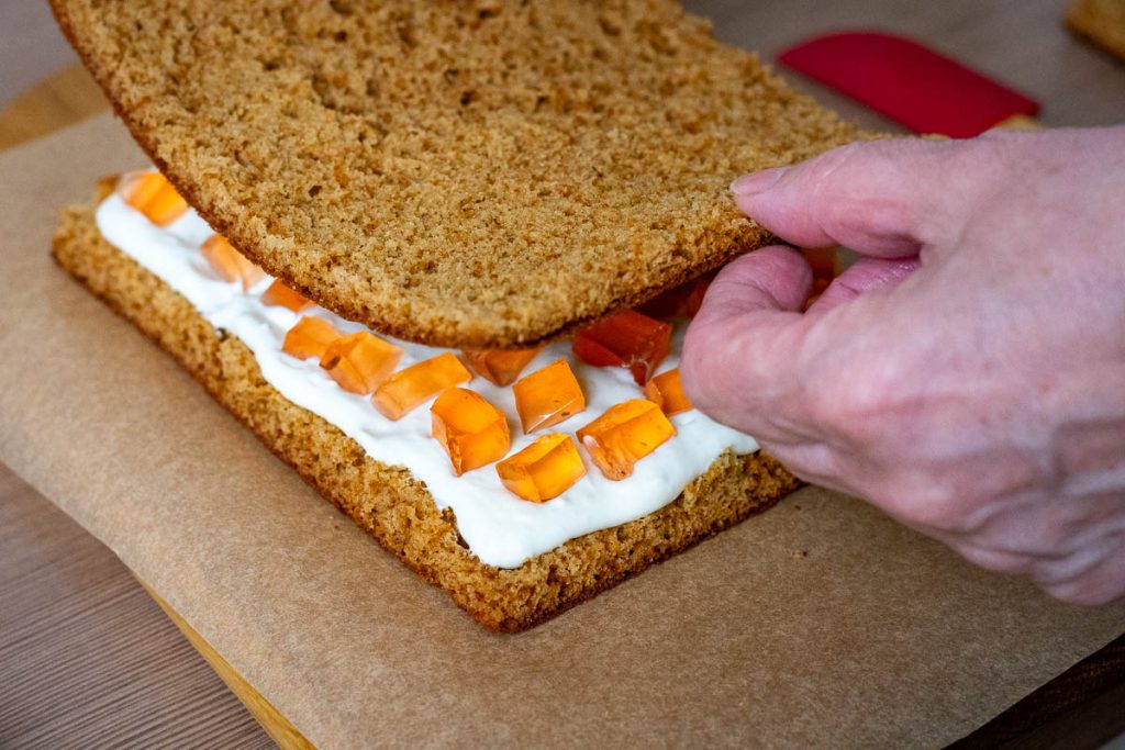Assembling Lithuanian Honey Cake Sodzius by layering sponge, sour cream filling and jelly cubes.