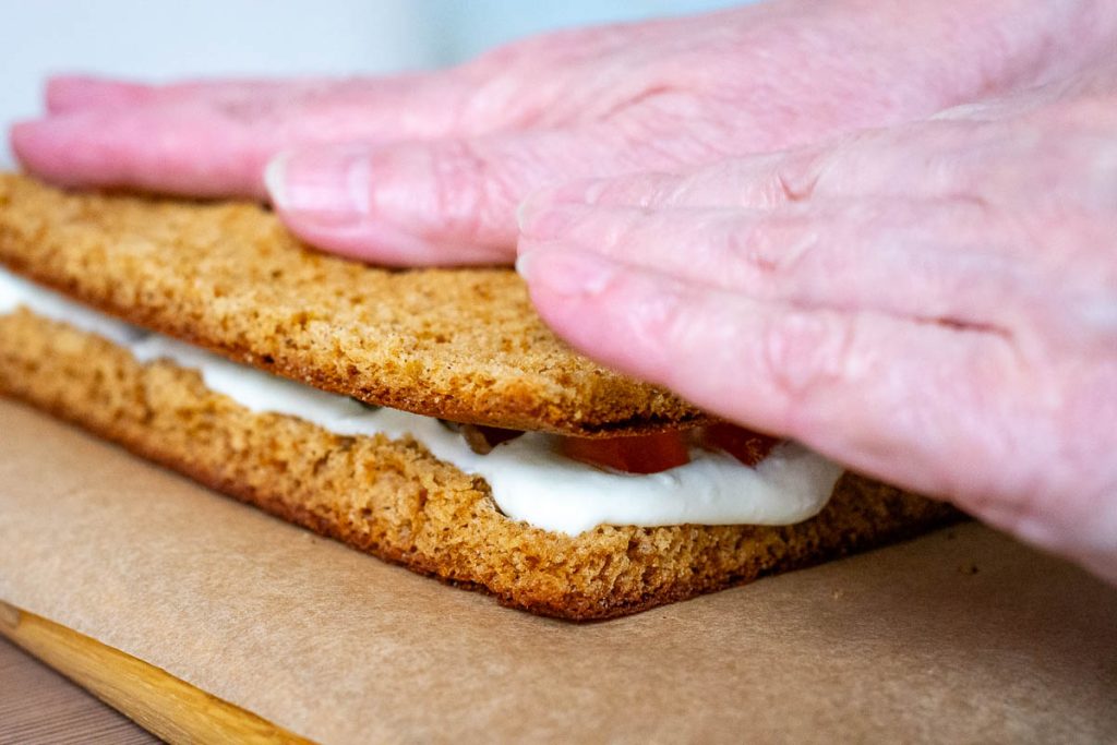 Assembling Lithuanian Honey Cake Sodzius by layering sponge, sour cream filling and jelly cubes.
