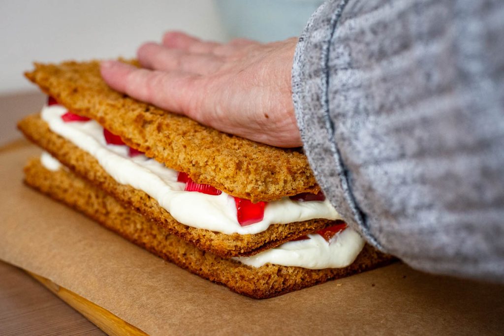 Assembling Lithuanian Honey Cake Sodzius by layering sponge, sour cream filling and jelly cubes.