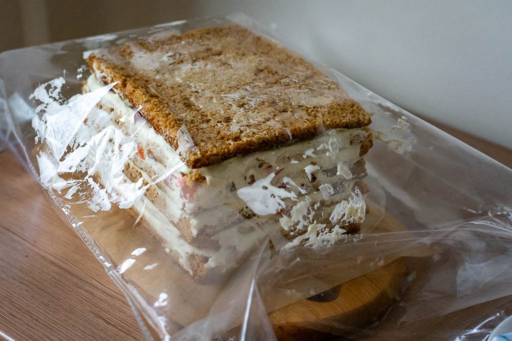 Assembled honey cake covered with plastic wrap.