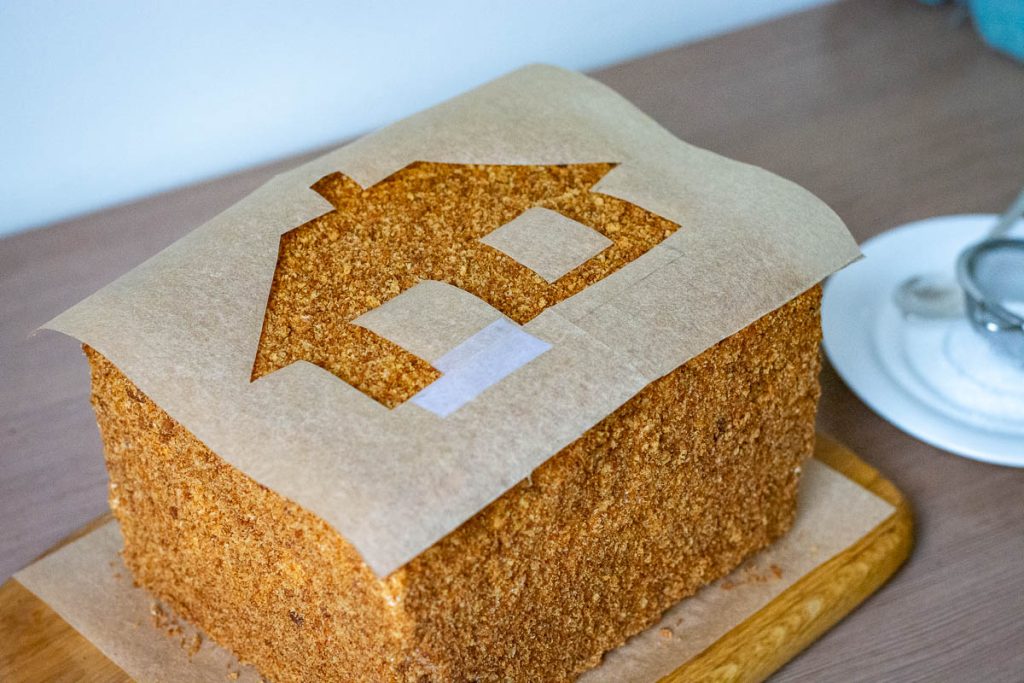 A stencil made from parchment paper showing a countryside house on top of the cake.