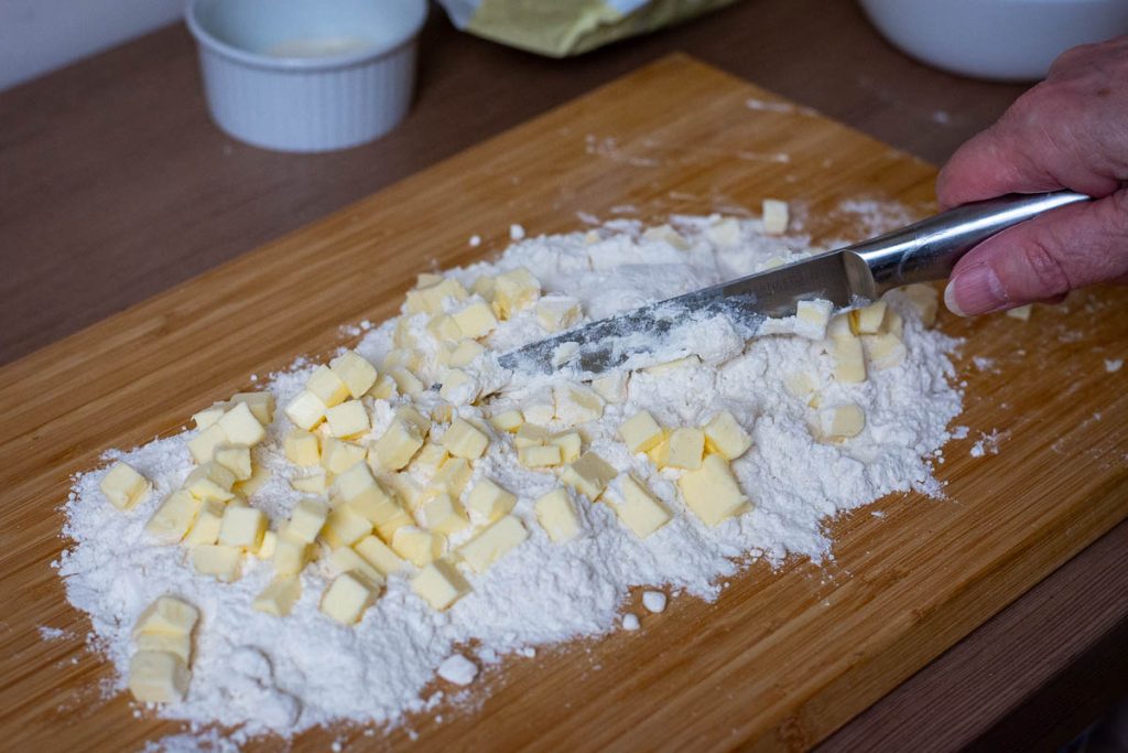 Chopping and slicing butter and flour on a large cutting board with a long bladed knife. 