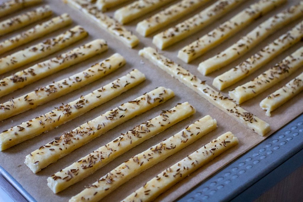 Lithuanian cheese straws arranged on a parchment paper lined baking sheet. 