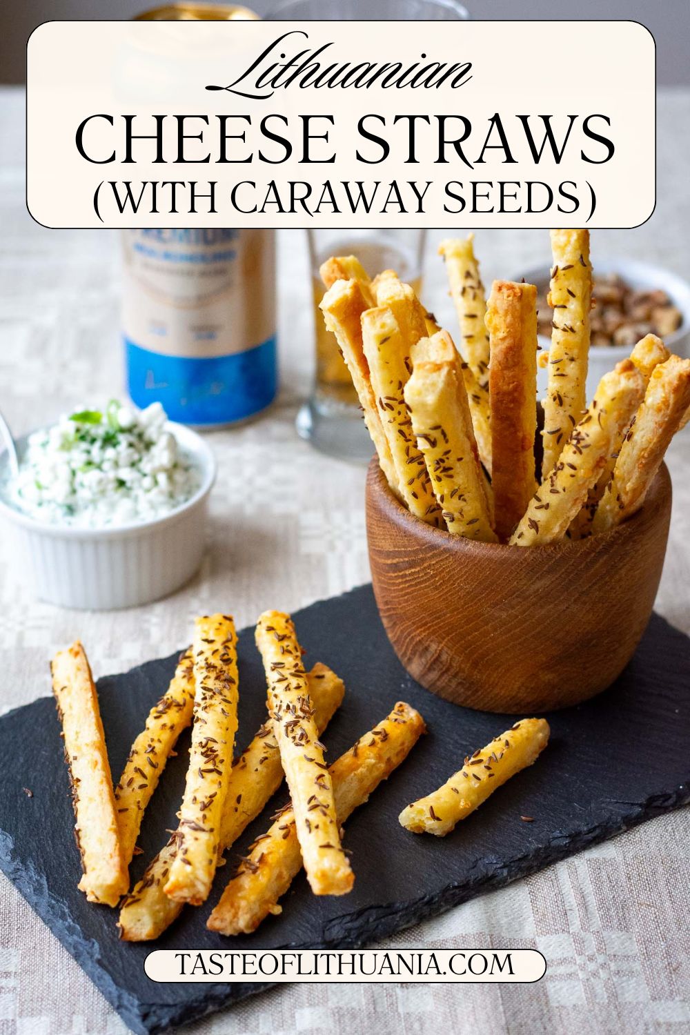 Lithuanian Cheese Straws with Caraway Seeds arranged on a black slate board with the rest of the cheese sticks in a wooden bowl. Pin for Pinterest. 