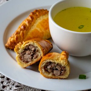 Lithuanian meat pies (known as kibinai) on a white plat with a bowlful of broth.