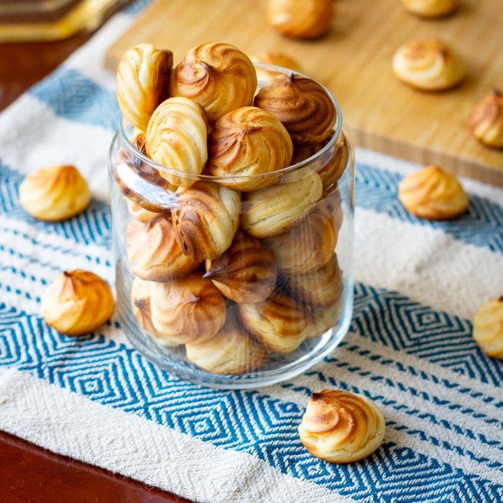 Lithuanian cookies, known as Plikyti Sausainiai, made with choux style pastry, in a glass jar on a kitchen towel.
